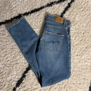 Blå Nudie jeans - Säljer ett par oanvända Jeans från Nudie i modellen Grim Tim med W30 och L32. Dessa jeans är stilsäkra och håller en hög kvalitet. Modellen är 187cm lång. Nypris ligger på 1600 tveka inte vid frågor eller prisförslag👖🌂🧵.