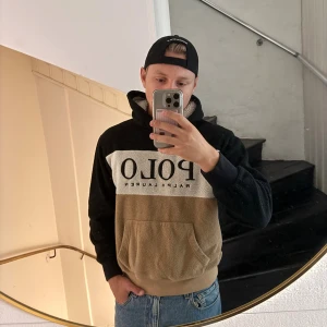 Polo Ralph Lauren hoodie i fleece - Säljer en sjukt skön hoodie från Polo Ralph Lauren i fleece. Tröjan är svart, beige och vit med stor POLO-logga framtill. Har huva, känguruficka och lång ärm. Perfekt för kalla dagar och riktigt snygg till jeans.