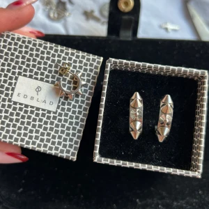 Edblad örhängen silver + en liten  - Coola silvriga hoops från Edblad med markerade nitar runt hela örhänget. De är i metall och har en edgy design som verkligen sticker ut. Perfekta för dig som vill ha ett smycke med attityd och unik känsla. Rostfritt stål är dessa + ett örhänge i samma modell fast liten för har bara ena till de paret