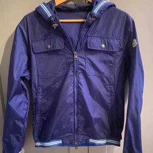 Blå vindjacka från Moncler  - Snygg och stilren blå vindjacka från moncler. Jackan är nästan aldrig använd och har inga skador eller fläckar. Den är i storlek 1 - Small