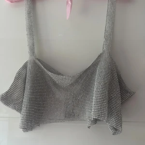 Ny. Glittrig silver croppad linnetopp WH - Säljer en glittrig croppad linnetopp från HM i silver med breda axelband. Toppen är täckt av små glittrande stenar som ger en riktigt festlig vibe. Materialet är syntet och toppen har en öppen rygg med kedja för stängning. Perfekt för att sticka ut i mängden! Storlek M/L