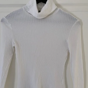 Vit ribbad polotröja från SHEIN - Säljer en vit ribbad polotröja från SHEIN i storlek S. Tröjan har lång ärm, hög polokrage och är tillverkad i ett stretchigt material som sitter snyggt på kroppen. Perfekt att styla med jeans eller kjol för en clean look.