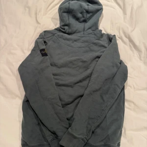 Mörkgrön hoodie från Stone Island - Säljer en mörkgrön hoodie från Stone Island med klassisk patch på vänster ärm. Tröjan har huva, känguruficka och långa ärmar. Perfekt för dig som gillar streetwear och vill ha en stilren look. Materialet är mjuk bomull som känns skönt mot huden.