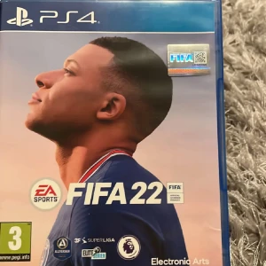 FIFA 22 PS4 - FIFA 22 till PlayStation 4 i mycket fint skick. Komplett med fodral, skiva och manual. Perfekt för fotbollsälskare som vill spela det senaste inom Ultimate Team och karriärläge. Skivan ser ut att vara i bra skick utan synliga repor.