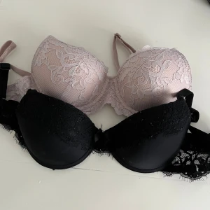 2 spetsiga push-up bh:ar svart & ljusrosa - Två bh:ar med push-up och spetsdetaljer, en i svart och en i ljusrosa. Båda har vadderade kupor och fina spetsmönster över hela framsidan samt justerbara axelband. Perfekt för dig som gillar en feminin och elegant look.