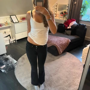 Svarta bootcut jeans med låg midja - Snygga svarta jeans med bootcut och låg midja. Jeansen har klassisk femficksdesign, dragkedja och knapp framtill. Modellen är figurnära upptill och släpper ut vid bensluten för en trendig siluett. Perfekta till sneakers eller boots.