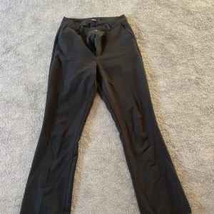 Svarta kostymbyxor med bootcut - Snygga svarta kostymbyxor  och klassisk passform. Byxorna har fickor fram och stängs med dragkedja och knapp. Perfekta för en stilren look och passar till många olika outfits.
