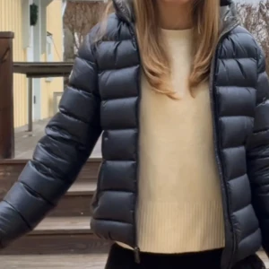 Svart Colmar pufferjacka med huva - Snygg svart/mörkblå pufferjacka från Colmar med glansig finish och huva. Jackan har quiltad design, dragkedja framtill och Colmar-logga på ärmen. Perfekt för kalla dagar och riktigt skön att bära. Passformen är normal och jackan är lätt att matcha med olika outfits.