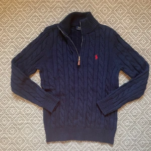 Marinblå stickad tröja Polo Ralph Lauren - Snygg mörkblå stickad tröja från Polo Ralph Lauren med half zip och kabelstickat mönster. Använd endast ett par gånger men sedan bilden togs har storlek lappen trillat av. Pris kan diskuteras vid snabb affär. Hör av dig vid några frågor
