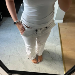 Vita cargopants med snörning - Säljer ett par vita cargopants med breda ben och dragsko i midjan. Byxorna har stora fickor fram och bak samt justerbar snörning vid benslut. Perfekta för en chill och avslappnad stil. Materialet känns lätt och luftigt.