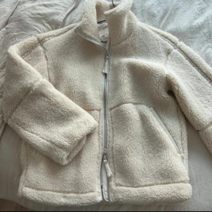 Vit teddyjacka från h&m - Mysig vit teddyjacka från H&M med hög krage och praktiska fickor framtill. 