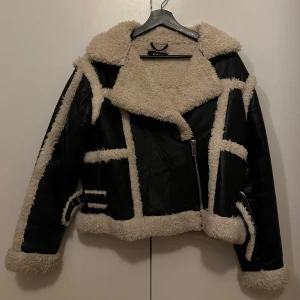 Svart teddyjacka från Gina Tricot XS - Säljer en svart teddyjacka från Gina Tricot i storlek XS. Jackan har krämvita teddy-detaljer längs kanter, krage och ärmar, samt bälten vid handlederna. Materialet är syntet med mjuk teddy och jackan stängs med dragkedja framtill🤍