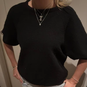 Svart kortärmad stickad tröja  - Svart stickad tröja från Lindex med korta ärmar och avslappnad passform. Materialet är stickat och har en lite ruff struktur som ger en cool känsla. Perfekt till jeans eller kjol för en enkel men snygg look.