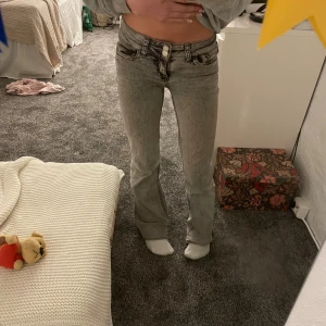 Grå bootcut jeans med låg midja - Säljer ett par gråa bootcut jeans från Nelly med låg midja. Dem är i storlek EU34 men dem är avklippta där nere så dem passar folk som är typ 151-156. Dem är även sudda där nere men det är inget man känner på. 