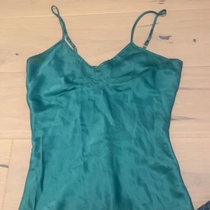 Grön sidenlinnetopp med smala axelband - Snygg grön linnetopp i siden med smala, justerbara axelband och lätt v-ringad hals. Toppens material ger en lyxig känsla och den har en figurnära passform som framhäver siluetten. Perfekt att styla med jeans eller kjol för en trendig look.