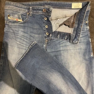 Diesel Buster ljusblå jeans W34 L32 - Säljer ett par Diesel Buster jeans i ljusblå tvätt med snyggt slitna detaljer. Modellen är regular slim tapered med stretch för extra komfort. Klassisk femficksdesign, knappgylf och diskret Diesel Industry-märke på myntfickan. Perfekta för en avslappnad streetstil.