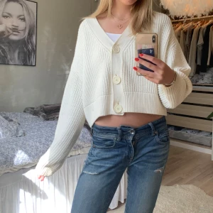 Vit stickad kofta - Säljer en superfin vit stickad kofta med stora knappar framtill. Den är croppad och har en loose passform. Passar perfekt till både jeans och kjol! (Bilderna från förra säljaren)