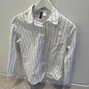 Vit randig skjorta från H&M Divided - Snygg vit skjorta från H&M Divided med svarta tunna vertikala ränder. 