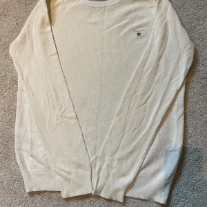 Vit bomullströja från GANT - Säljer en stilren vit långärmad tröja från GANT i 100% bomull. Tröjan har rund halsringning, diskret struktur i tyget och GANT-logga broderad på bröstet. Perfekt för dig som gillar klassisk och clean stil.