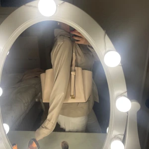 Beige axelväska från Nine west - Snygg beige axelväska i stilren design. Väskan har en strukturerad form, justerbart axelband och gulddetaljer. Perfekt storlek för att få plats med allt du behöver och passar till många olika outfits.