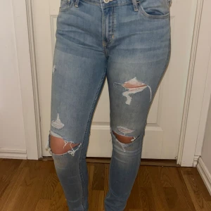 Ljusblå ripped jeans från Hollister - Säljer ett par ljusblå skinny jeans från Hollister med slitningar och hål vid knäna. Jeansen har klassisk femficksdesign, låg midja och är tillverkade i stretchig denim för en tight passform. Xs/S