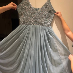 Ljusblå långklänning Boohoo Occasion - Magisk ljusblå långklänning från Boohoo Occasion med v-ringning och tunna axelband. Överdelen är täckt av glittriga paljetter i blommigt mönster och kjolen är i flera lager av mjuk, flowy tyll. Perfekt för bal eller speciella tillfällen! Storlek UK18 motsvarar storlek EU46. Köpt för 1200kr