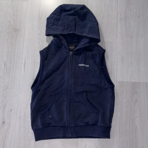 Mörkblå hoodieväst från Iets Frans - Snygg mörkblå hoodieväst från Iets Frans med dragkedja framtill och två fickor. Västen har en stor huva och broderad logga på bröstet. Perfekt för lager-på-lager och chill stil. Materialet är mjuk bomull som känns skönt mot huden. Nypris 449