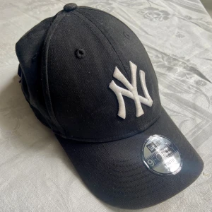 Svart New Era Yankees keps 9FORTY - Snygg svart keps från New Era med klassiskt New York Yankees-broderi i vitt framtill. Modellen är 9FORTY Youth Adjustable med böjd skärm och justerbar passform. Perfekt accessoar för en sportig och urban stil.