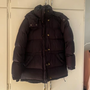 Svart dunjacka från Boomerang S - Säljer en svart dunjacka från Boomerang i storlek S. Jackan har en hög krage, huva och stora fickor framtill. Stängs med både dragkedja och knappar. Perfekt för kalla dagar med sin fluffiga och varma känsla. Klassisk och stilren design som funkar till det mesta.