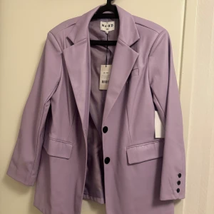 Oversized Kavaj från NA-KD i lilla färg - Snygg oversized kavaj fràn NA-KD i lila färg. Kavajen har klassisk krage, tvà framfickor med lock, bröstficka och knappar i mörk ton pả ärmslut och framtill. Materialet är twill och insidan är fodrad i matchande lila. Perfekt för dig som vill sticka ut. 