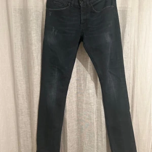 Svarta Dondup jeans  - Snygga svarta jeans från Dondup med diskreta slitningar och klassisk femficksdesign. Jeansen har en smal siluett och mörk tvätt, med metall-D detalj vid fickan och läderpatch med logga bak. Perfekta för dig som gillar stilrena och moderna jeans.