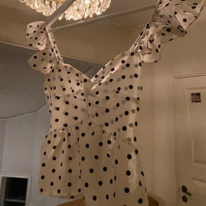 Prickig vit topp med volang - Supersöt vit topp med svarta prickar och volangdetaljer på axelbanden. Jättebra festtopp!