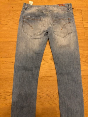 Ljusblå skinny jeans från Dondup - Snygga ljusblå jeans från Dondup, modellen har en slim och skinny passform med klassisk femficksdesign, knappgylf och subtila slitningar. Jeansens material är mjukt och stretchigt denim med bruna sömmar och en broderad logga bak.