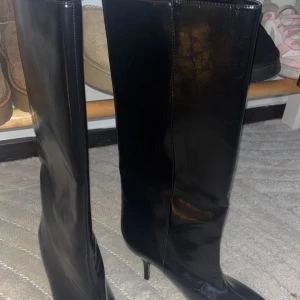 Svarta höga stövlar med klack Från Zara - Säljer ett par svarta, glansiga stövlar med spetsig tå och smal klack. Stövlarna är höga och har en stilren, minimalistisk design. Materialet är skinnimitation som ger en snygg finish. Perfekta för dig som vill ha en edgy look med lite extra höjd.Prislapp kvar 