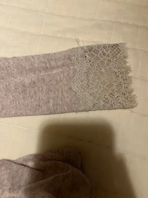 Beige långärmad topp med spets från Intimissimi (S) - Superfin beige långärmad topp från Intimissimi med v-ringning och detaljerad spets runt halsen och ärmsluten. Mjuk och tunn kvalitet med kashmirblandning, perfekt för dig som gillar en feminin och chill stil.