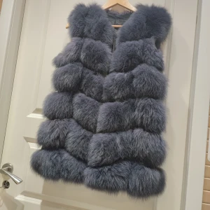 Mörkgrå fluffig pälsväst - Säljer en riktigt fluffig och lyxig pälsväst i mörkgrå ton. Västen har en voluminös och mjuk look med breda horisontella sektioner av päls. Perfekt för dig som vill sticka ut och hålla dig varm med stil. Ingen synlig knäppning eller dragkedja framtill.