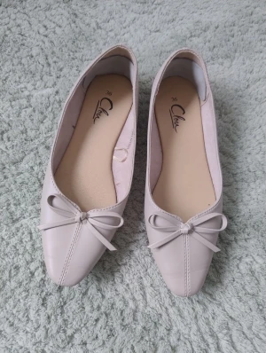 Beige ballerinaskor med rosett  - Snygga ballerinaskor från Clou i beige färg med spetsig tå och dekorativ rosett framtill. Skorna har en platt sula och är tillverkade i syntetmaterial med mjuk innersula för extra komfort. Endast använda en gång.