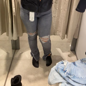 Grå ripped jeans med slits - Snygga grå jeans med slitningar och hål över knäna, samt slits vid bensluten. Jeansen har en klassisk femficksdesign och är i en rak passform som sitter bekvämt. Pis kan diskuteras