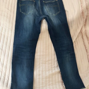 Slim fit jeans blå 31/32 - Slim fit jeans i mörkblå tvätt med snygga slitningar och klassiska fem fickor. Jeansen har en smal passform och rå kant vid benslutet för en cool look. Tillverkade i jeansmaterial med kontrastsömmar.