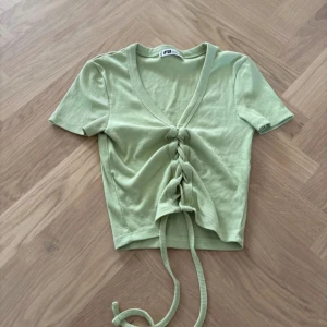 Ljusgrön ribbad topp från FB Sister - Säljer en ljusgrön ribbad topp från FB Sister i storlek XXS. Toppen har korta ärmar, v-ringning och snygg snörning framtill som ger en croppad look. Perfekt för dig som gillar trendiga detaljer och mjuka material.