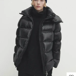 Massimo Dutti jacka  - Säljer en svart pufferjacka med stor, mysig huva och breda, quiltade kanaler. Jackan har en glansig finish, två sidofickor med dragkedja och hel dragkedja framtill. Perfekt för kalla dagar och riktigt snygg till streetwear-stilen.