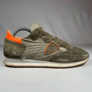 Philippe Model sneakers olivgrön orange - Snygga sneakers från Philippe Model i olivgrönt med detaljer i orange. Skorna har en rund tå, snörning och platt sula. Materialmix av mocka och syntet med mesh framtill och kontrasterande orange häl. Perfekt för dig som gillar streetstyle och unika färgkombinationer. 