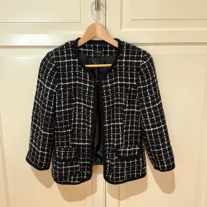 Svart rutig kavaj från Lindex - Snygg svart kavaj från Lindex i storlek 36  med vit rutigt mönster. Jackan har rundad hals, två fickor framtill och är helfodrad.  OBS Det står att den är storlek 40 men den är extremt liten i storleken så det är storlek 36