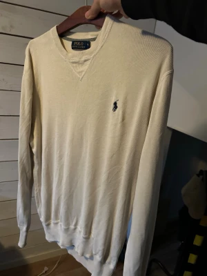 Beige tröja från Polo Ralph Lauren - Snygg beige långärmad tröja från Polo Ralph Lauren med klassisk broderad logga på bröstet. Tröjan har rund halsringning och ribbade muddar vid ärmslut och nederkant. Perfekt för lager-på-lager och stilrena outfits.