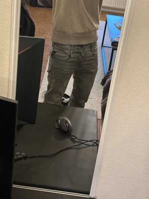 Grå replay  jeansbyxormed raka ben - Säljer ett par grå replay jeansbyxor med raka ben och snygga detaljer på bakfickorna. Byxorna har klassisk femficksdesign, bälteshällor och en stilren look som passar till det mesta. Materialet är jeans och färgen är en ljusgrå ton.