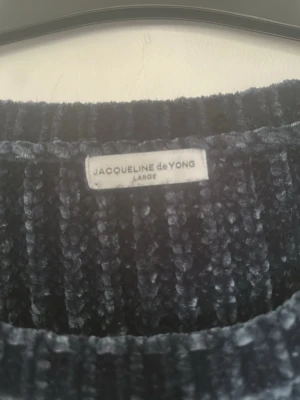 Mörkblå ribbad tröja Jacqueline de Yong - Mysig mörkblå ribbad tröja från Jacqueline de Yong i storlek Large. Tröjan har lång ärm och är gjord i ett mjukt, glansigt material som känns lyxigt mot huden. Perfekt för kyliga dagar när du vill vara både bekväm och snygg.