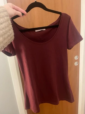 Vinröd t-shirt från Anna Field - Snygg vinröd t-shirt från Anna Field med rund, djup urringning och korta ärmar. Modellen är figurnära och enkel utan mönster eller detaljer. Perfekt till jeans eller kjol💕 endast använd en gång!!