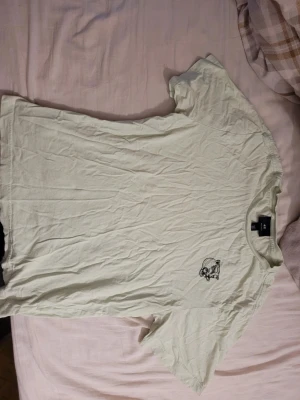 Vit t-shirt med tryck från H&M - Enkel vit t-shirt från H&M med ett litet svart tryck av ett djurhuvud på bröstet. Klassisk rund halsringning och korta ärmar. Tillverkad i mjuk bomull som känns skön mot huden. Perfekt till jeans eller shorts.