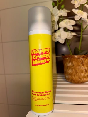Happy Crazy Mine Heat Protection - Säljer en färgglad sprayflaska från Happy Crazy Mine med gul etikett och röd text. Produkten är en värmeskyddsspray för håret och kommer i en smidig plastflaska med matt lock. Perfekt för dig som vill skydda håret mot värmeverktyg.