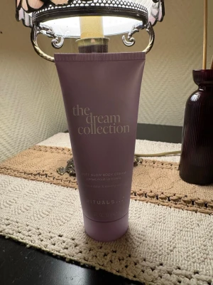 The Dream Collection body cream Rituals - Oöppnad. Lila tub med The Dream Collection Soft Glow Body Cream från Rituals. Innehåller doft av blue daisy och moonstone. Tuben rymmer 100 ml och har en stilren, matt finish med silverfärgad text.